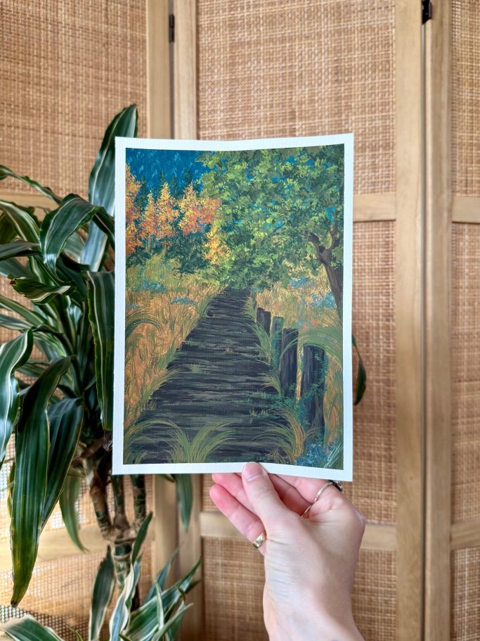 Eine Person hält ein bunten Kunstwerk eines Weges durch eine herbstliche Landschaft.