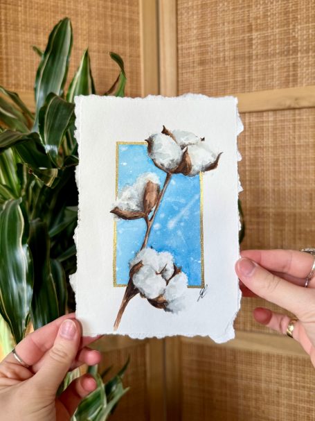 Karte mit Baumwollzweigen vor einem blauen Hintergrund, in Händen gehalten.