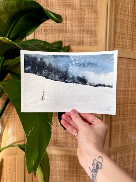 Eine Hand hält eine winterliche Landschaft mit Schnee und einem stürmischen Himmel.