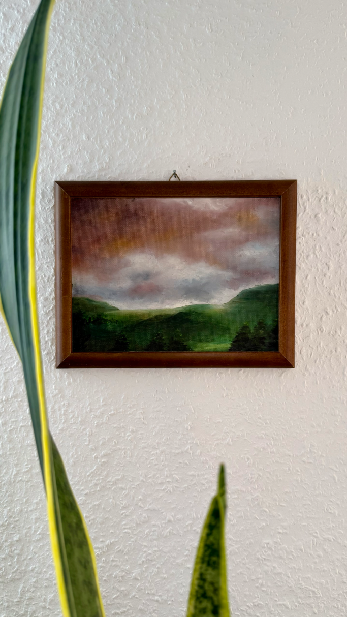 Landschaftsgemälde in einem Holzrahmen, grüne Felder und bewölkter Himmel.