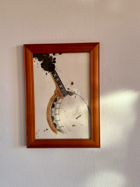 Gemaltes Banjo in einem Holzrahmen, umgeben von Tinte und kleinen Flecken.