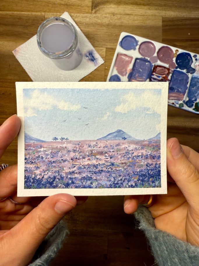 Eine Person hält eine Landschaftsskizze mit Bergen und blassem Himmel in den Händen.