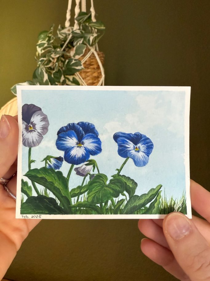 Hände halten eine Karte mit Blumenmotiven, hauptsächlich blauen Stiefmütterchen.