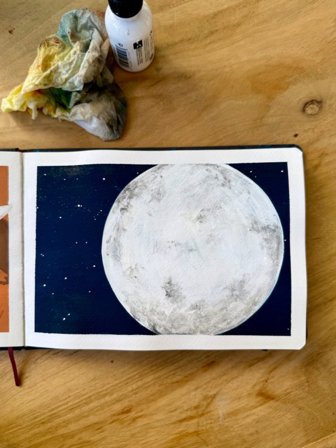 Vollmond auf dunklem Hintergrund in einem Skizzenbuch, neben Materialien.