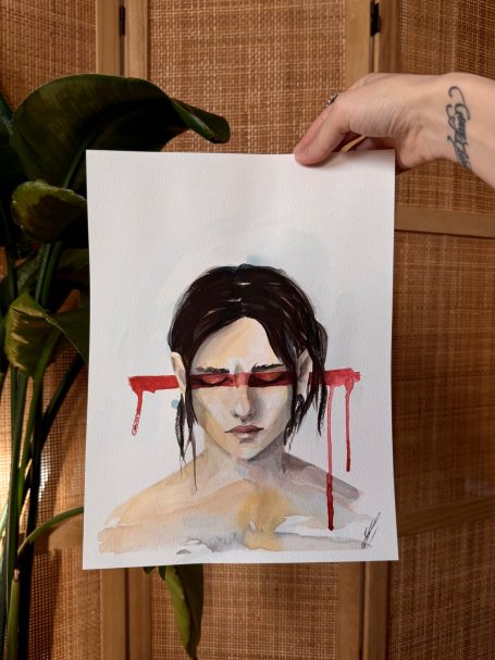 Porträt einer Frau mit rotem Augenmake-up und blutähnlichen Tropfen, vor einem Hintergrund aus Holz.