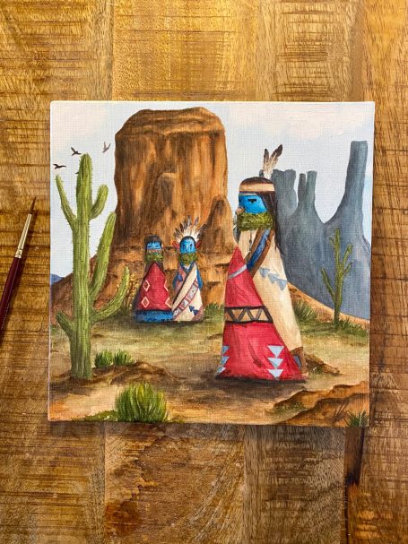 Drei Personen in traditioneller Kleidung vor einem Felsen in einer Wüstenlandschaft.