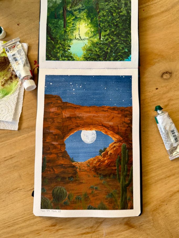 Ein offenes Skizzenbuch mit einer Waldszene und einem Felsenbogen bei Nacht.